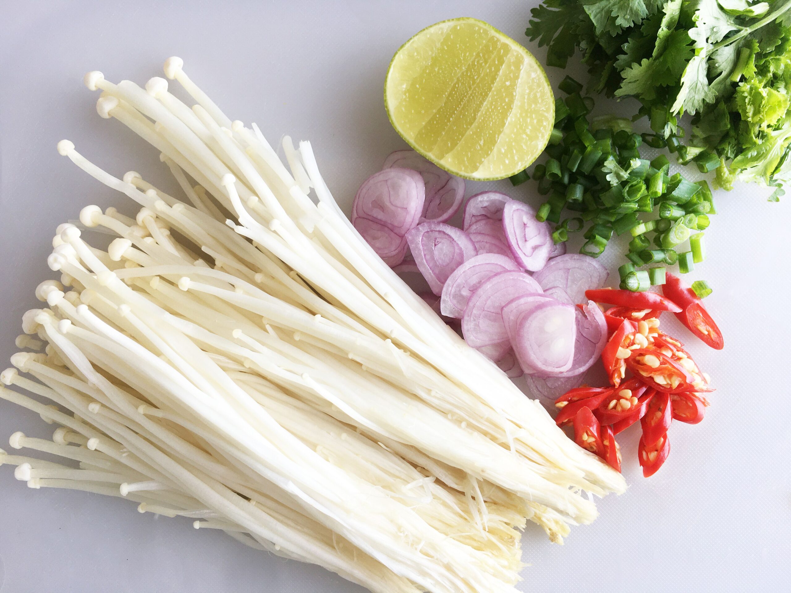 エノキをベースに３種類のカットされた野菜が白いまな板に置かれているイメージ